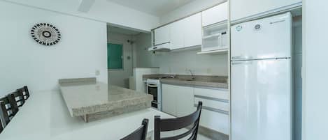 Uma cozinha compacta com armários brancos, micro-ondas embutido, geladeira de aço inoxidável e um espaço de refeições com mesa e cadeiras.