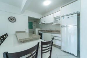 A compact kitchen with white cabinets, a built-in microwave, a stainless steel refrigerator, and a dining area with a table and chairs.