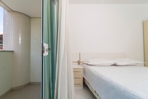 A bedroom with a bed, a bedside table, and a curtain partially drawn.