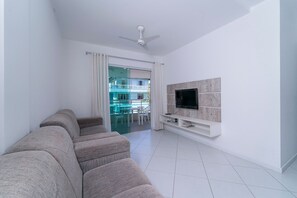 A modern living room with a sofa, a TV mounted on a wooden panel, and a ceiling fan.