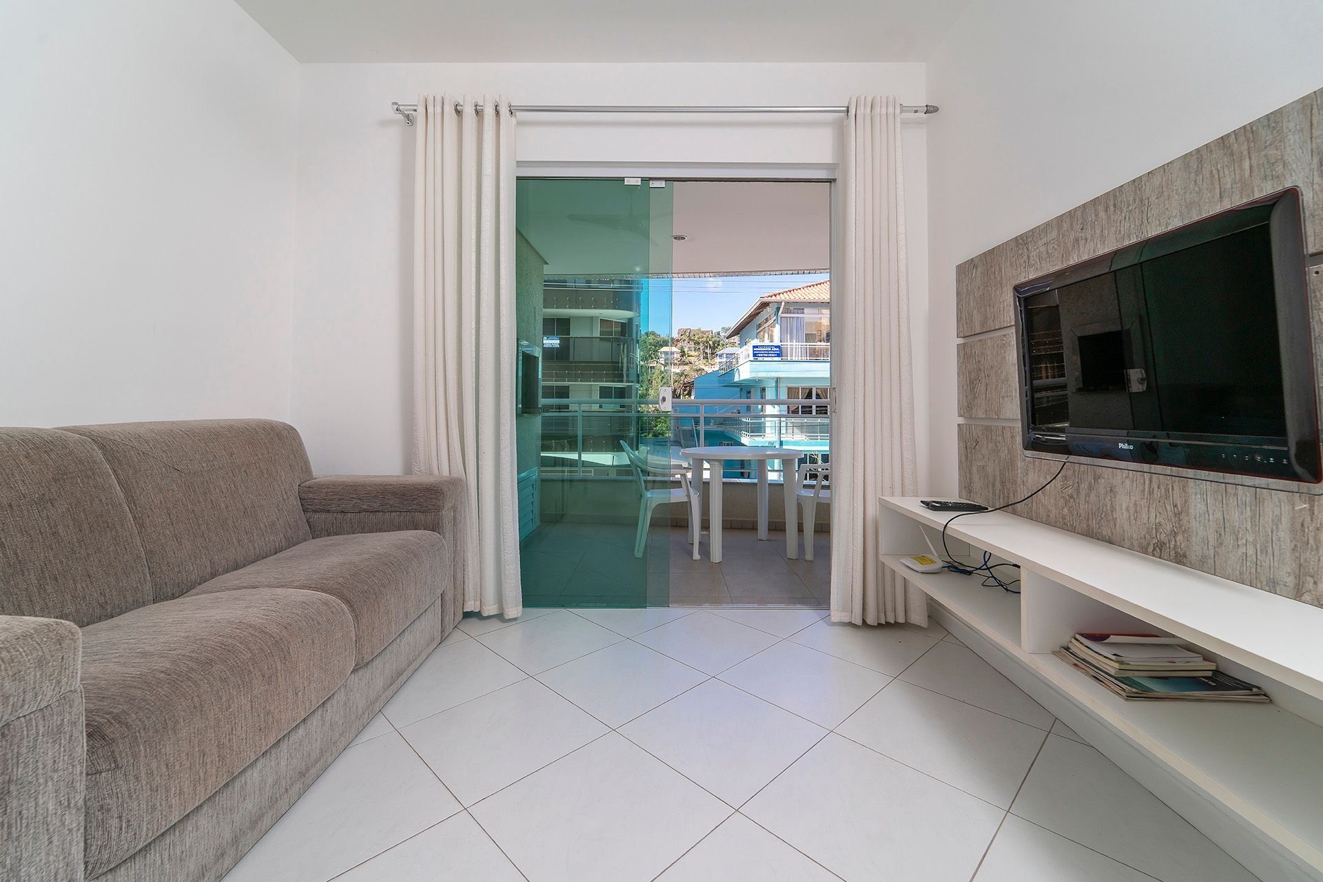 A living room with a sofa, a TV, and a glass door leading to a balcony with a table and chairs.