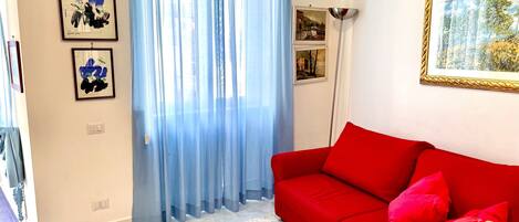 Un soggiorno con un divano rosso, una tenda blu e opere d'arte incorniciate alle pareti.