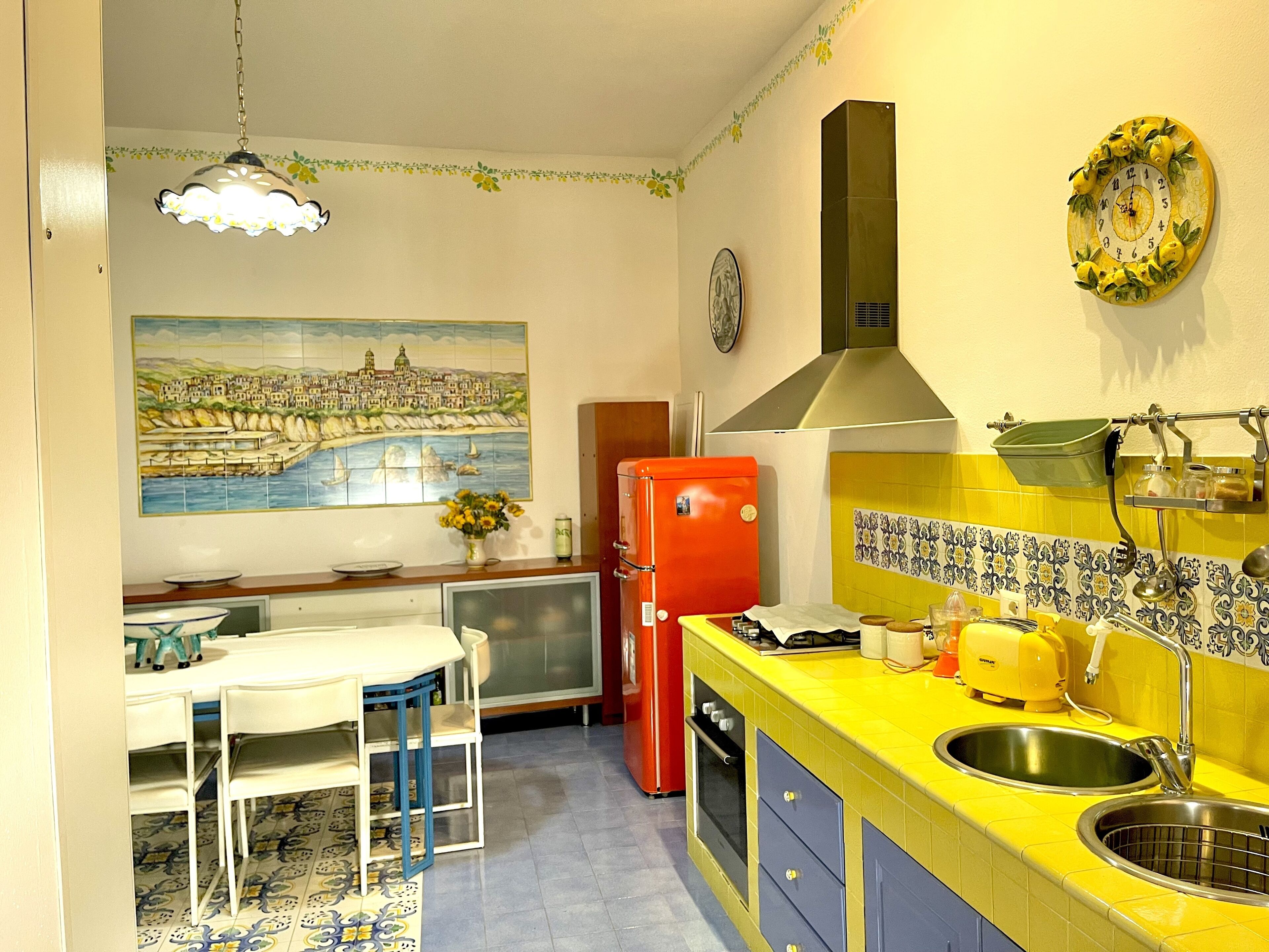 A kitchen with a yellow countertop, a red refrigerator, a stove, and a sink.