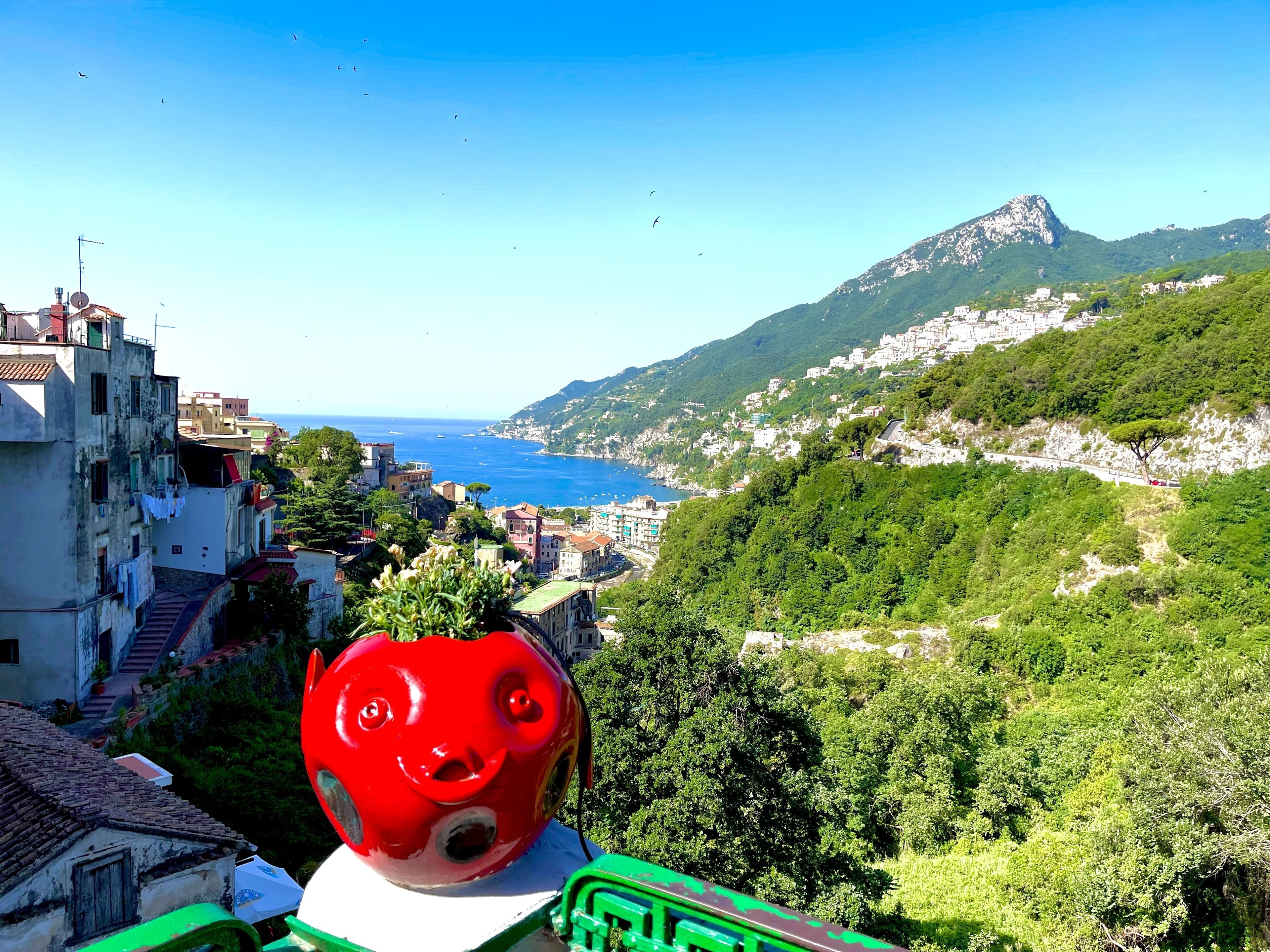 Un pueblo costero con edificios, una montaña y una escultura roja.