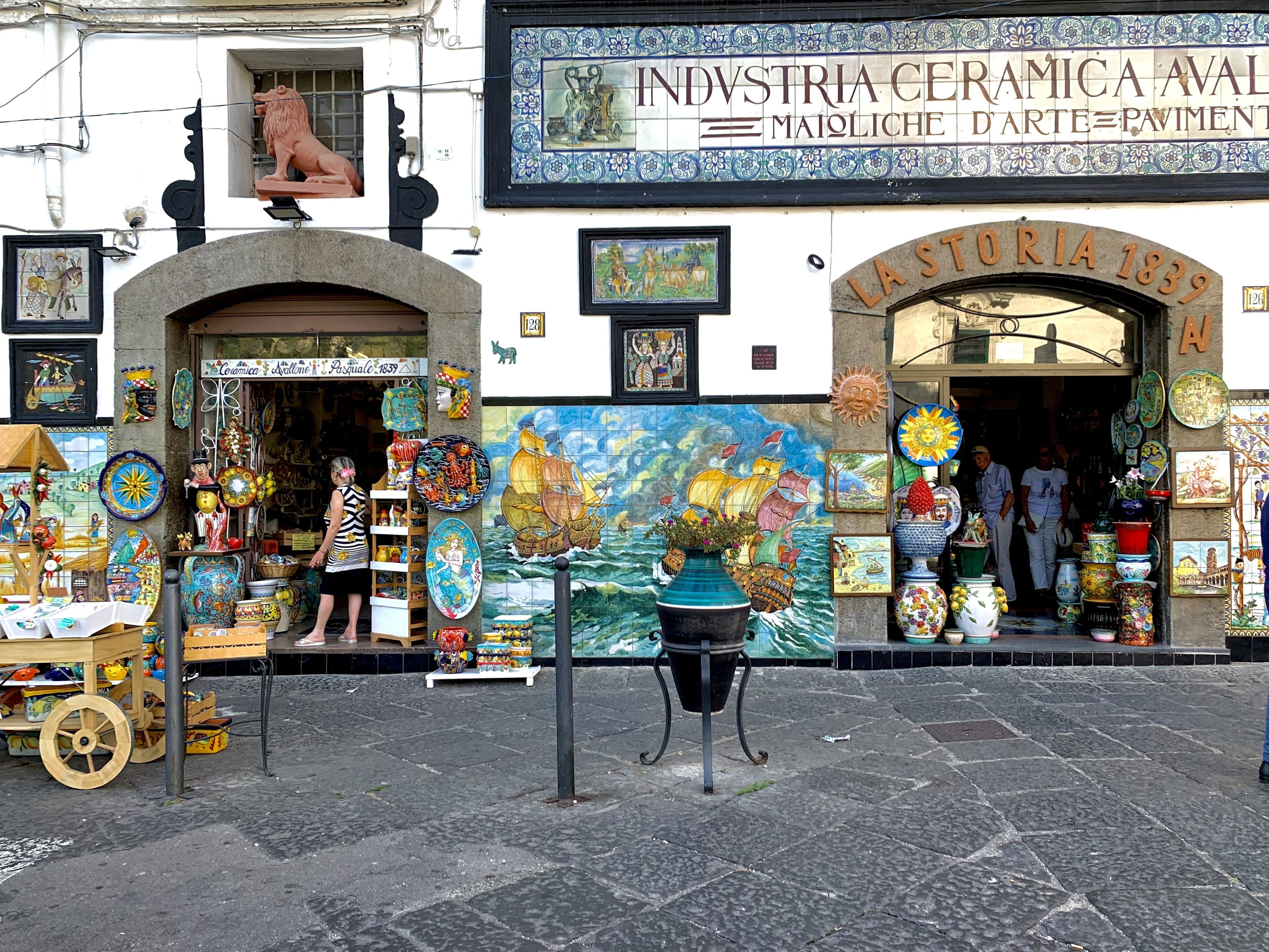 En keramikbutik med en lejonstaty, färgglada kakelplattor och en skylt med texten: ”INDUSTRIA CERAMICA AVAL MAIOLICHE D’ARTE PAVIMENT”.