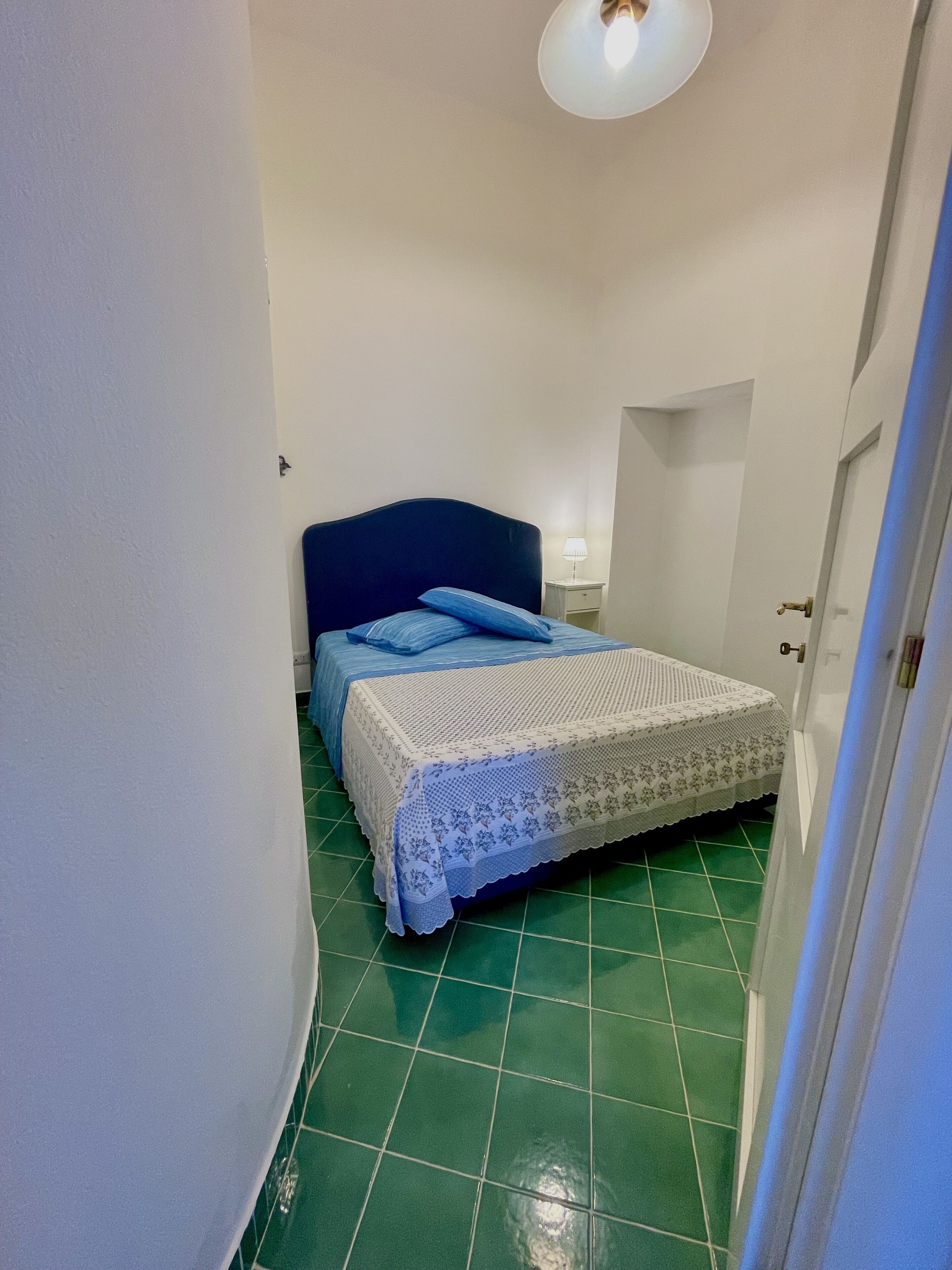 A narrow room with a bed, a nightstand, and a door.