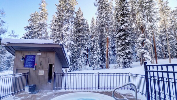 A wooden deck with a hot tub surrounded by snow-covered trees. - Rare Gem, Spacious Condo, Outstanding Location A6 (Copper Mountain)