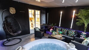 A modern indoor pool area with a hot tub, lounge seating, and a large window.