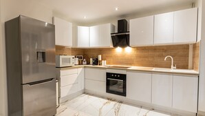 A modern kitchen with white cabinets, a stainless steel refrigerator, a built-in oven, and a wooden backsplash.