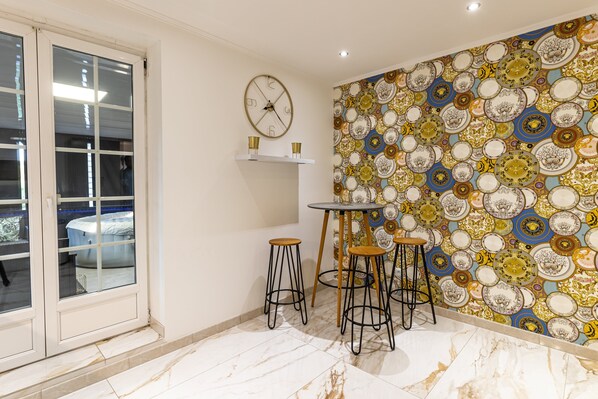 Une pièce avec un mur orné de motifs, une horloge et une petite table avec des tabourets.