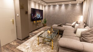 A modern living room with a sofa, a glass coffee table, and a flat-screen TV mounted on the wall.