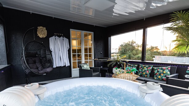 A hot tub area with a black wall, a white robe rack, a hanging chair, and a view of the outdoors.