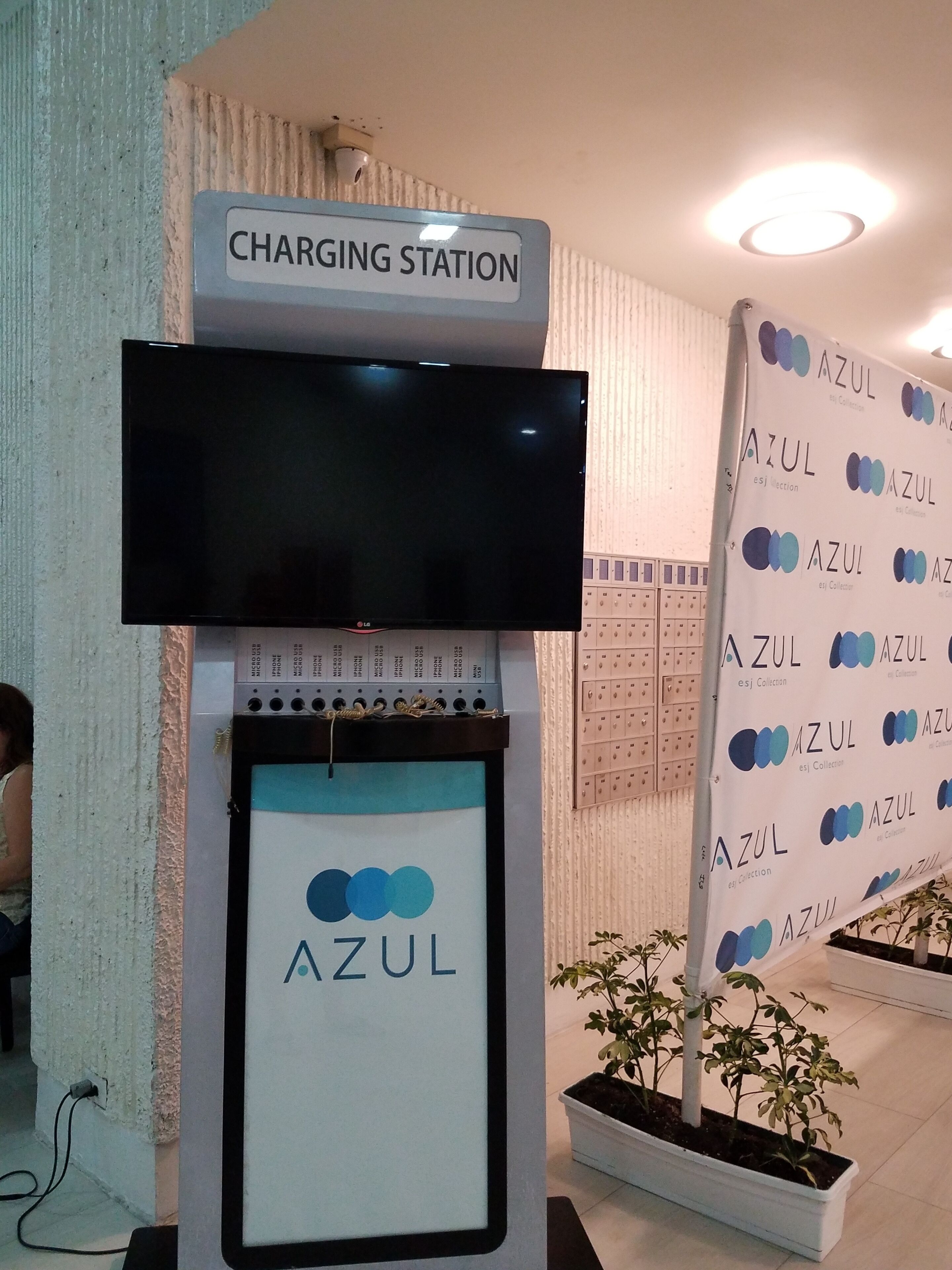 A charging station with a flat-screen TV above it, a sign with the word 'AZUL,' and a wall with a repeating pattern of the AZUL logo.