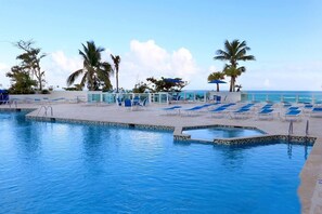 Zona de piscina con sillas de descanso y palmeras, con vista al océano.