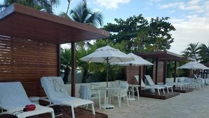 A poolside area with lounge chairs and umbrellas, surrounded by palm trees and a wooden pergola. - Beach HotelCndo 1562 (Carolina)