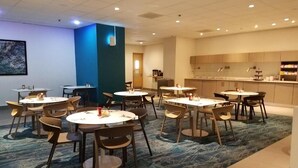 A hotel dining area with round tables and chairs, a kitchen in the background, and a blue accent wall. - Beach HotelCndo 1562 (Carolina)