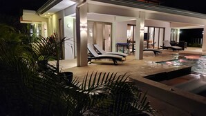 Een modern huis met een zwembad, lounge stoelen en een goed verlicht terras.