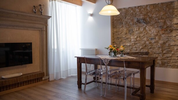 A dining area with a stone wall, wooden ceiling beams, a fireplace, and a table with chairs. - Margherita (Roè Volciano)