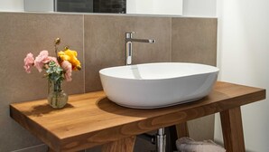 A modern bathroom with a wooden vanity, a white vessel sink, and a mirror above it. - Margherita (Roè Volciano)