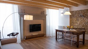 A living room with a fireplace, TV, dining table, and clear chairs. - Margherita (Roè Volciano)
