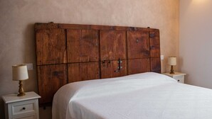A bedroom with a wooden headboard, a large bed, two bedside tables with lamps, and a wall-mounted light fixture. - Margherita (Roè Volciano)
