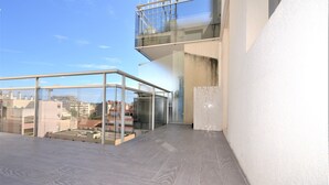 Eine Dachterrasse mit Glasbrüstung, Blick auf die Stadtlandschaft und einem gefliesten Boden.