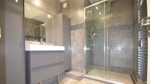 Ein modernes Badezimmer mit einer gläsernen Duschkabine, einem Waschtisch mit Spiegel und einem gefliesten Boden.