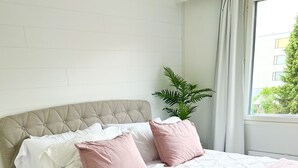 Una cama bien hecha con un cabecero acolchado, ropa de cama blanca y almohadas rosas.