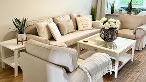 Una sala de estar con un sofá color beige, una mesa de centro de vidrio y un ventilador de techo.