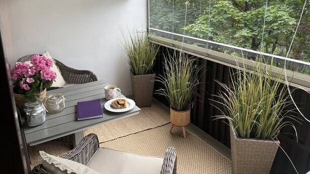 Un balcón acogedor con mobiliario de mimbre, plantas en macetas y vistas de vegetación exuberante.