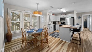 Een moderne keuken met een eethoek, met een centraal kookeiland, houten vloeren en een hanglamp.