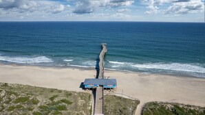 Een strand met een steiger die in de oceaan uitloopt, een heldere lucht en een zandstrand.