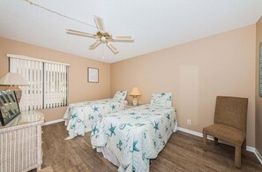 A bedroom with two beds, a ceiling fan, a chair, and a window with blinds.