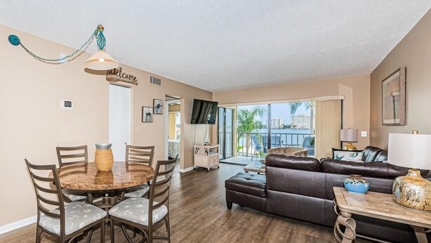 A spacious living room with a dark leather sofa, a wooden coffee table, and a dining area with a round table and chairs. - Waterfront 2BR/2BA condo with pool, hot tub, balcony, and Wi-Fi. (St. Petersburg)