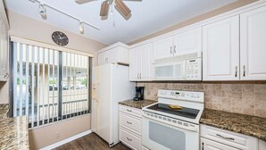 A kitchen with white cabinets, a microwave, a stove, and a clock on the wall. - Waterfront 2BR/2BA condo with pool, hot tub, balcony, and Wi-Fi. (St. Petersburg)
