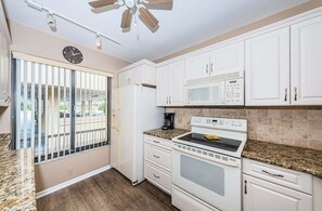 Una cocina con gabinetes blancos, microondas, estufa y un reloj en la pared.