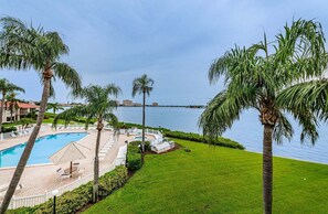 Área de piscina en un resort con palmeras, vista al mar y césped cuidado.