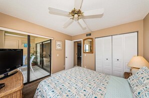 Une chambre à coucher comprenant un lit, un téléviseur, un ventilateur de plafond et une porte-fenêtre coulissante donnant sur un balcon.
