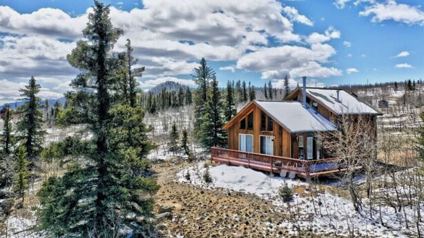 Eine Holzhütte mit Balkon, umgeben von verschneitem Gelände und immergrünen Bäumen.
