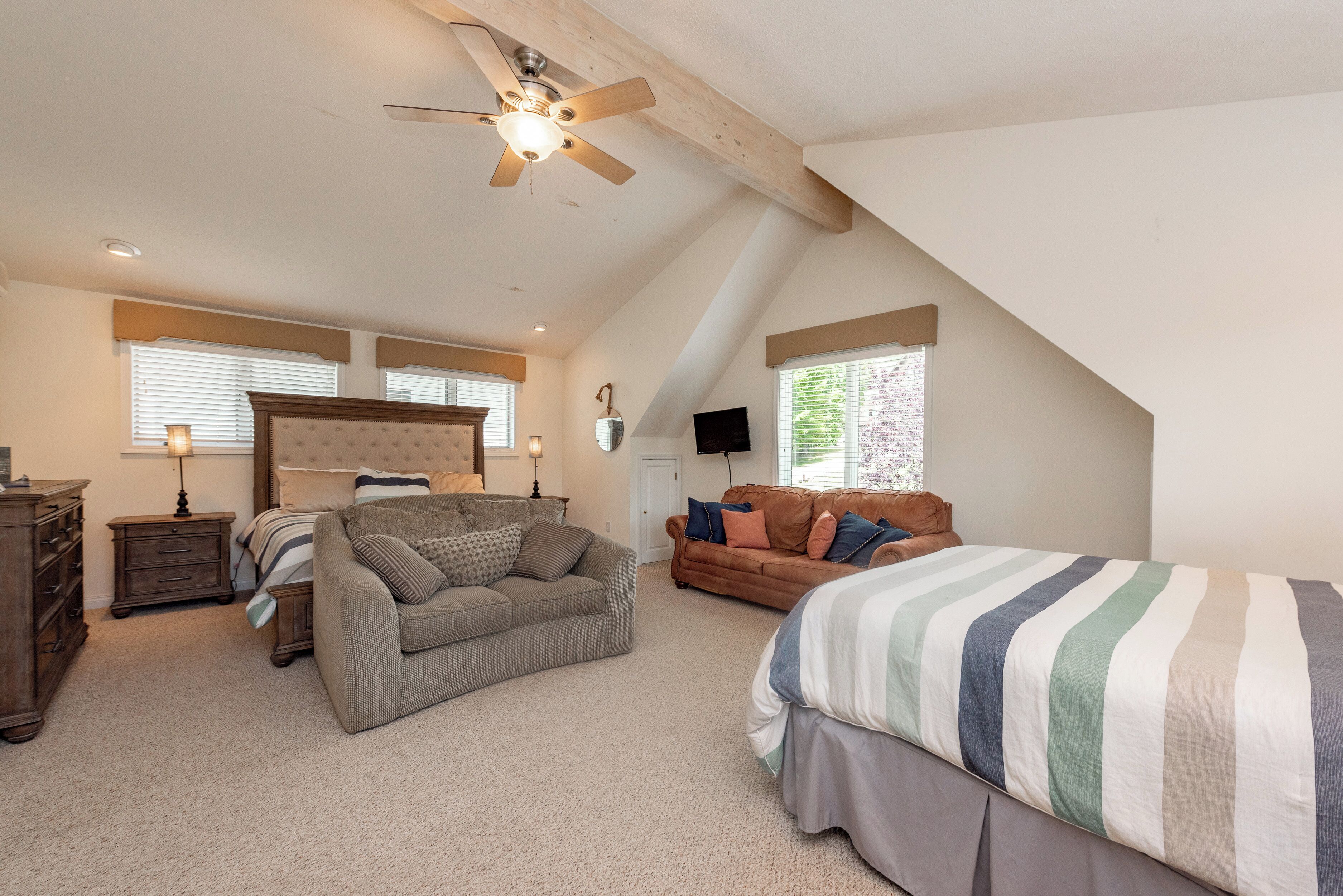 Ein Schlafzimmer mit schrägem Dach, einem Bett, einer Couch und einer Kommode.