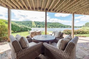 Un área de estar al aire libre techada con muebles de mimbre y vistas a un lago y colinas.