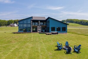 Een modern huis met twee verdiepingen, grote ramen, een stenen open haard en een terras met buitenmeubels.