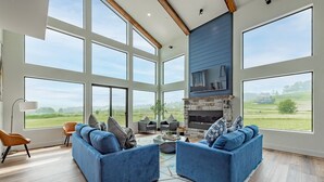 A spacious living room with large windows, a stone fireplace, and modern furniture. - Modern Dog Friendly Lake Retreat w/ Pool (Swanton)