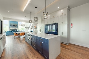 Een moderne keuken met een groot eiland, donkere kastjes en hanglampen.