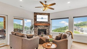 Un salón amplio con chimenea, ventanas grandes que ofrecen una vista panorámica y un ventilador de techo.