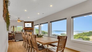 Un comedor amplio con una mesa y sillas de madera, ventanas grandes que ofrecen vistas del paisaje, y una chimenea de piedra.