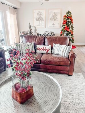 A living room with a brown leather sofa, a glass coffee table with a red floral arrangement, and a Christmas tree in the background. - Enjoy Idle Time at Table Rock Lake with Arcades, Private Hot Tub, Dog-Friendly Stay & Free Tickets (Branson)