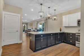 A modern kitchen with a large island, dark cabinetry, and pendant lighting.