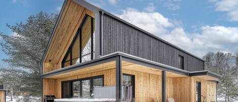A modern two-story house with a sloped roof, large windows, and a wooden exterior.