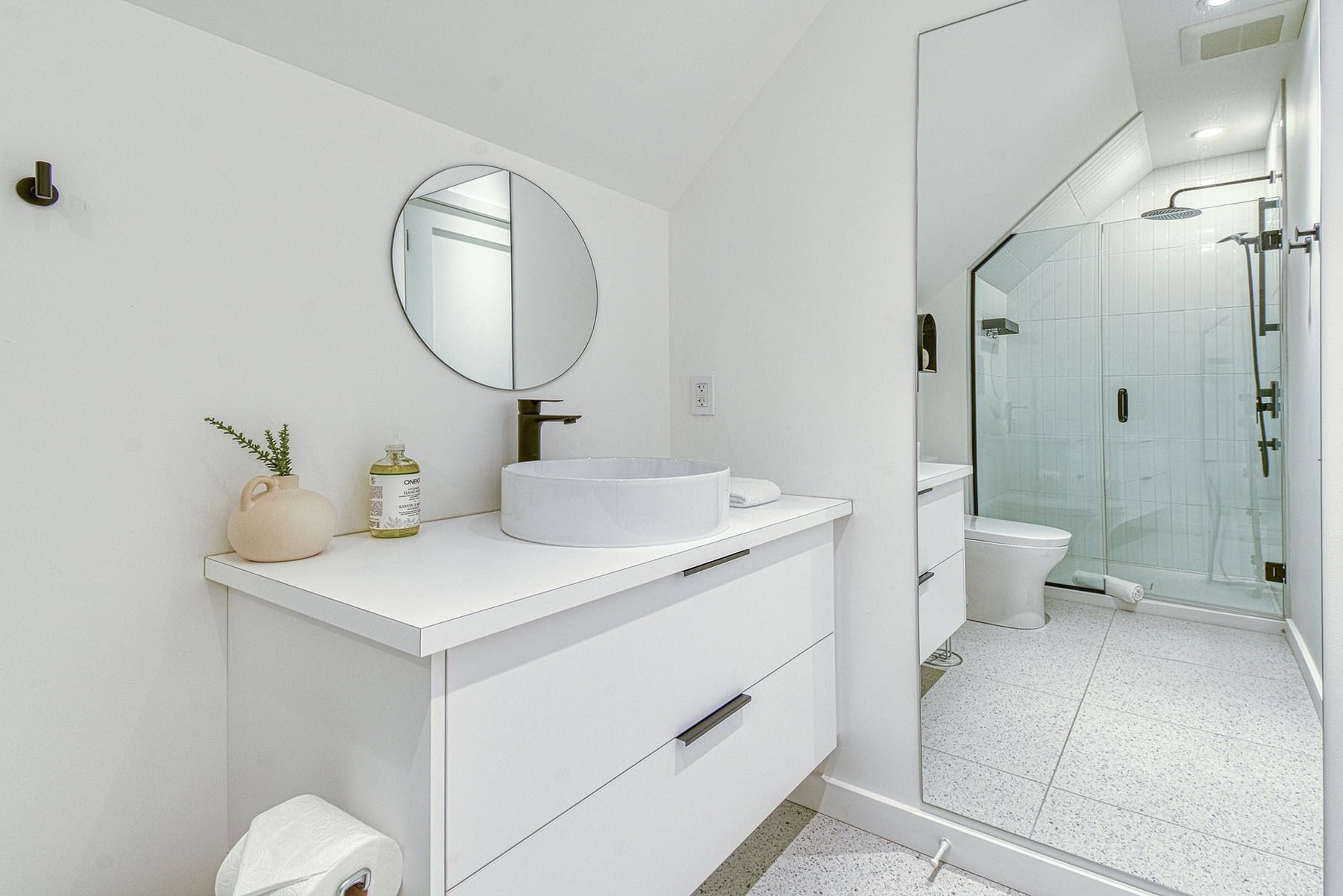 A modern bathroom with a white vanity, a round mirror, a sink, and a glass-enclosed shower area.